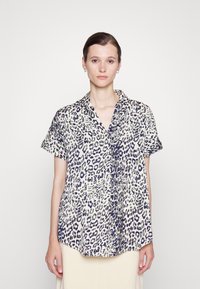 Camisa de manga curta, com colarinho, em padrão de estampado de leopardo. O tecido parece leve com uma base creme e manchas azul escuro e verde.