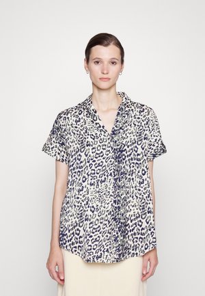 Camisa de manga curta, com colarinho, em padrão de estampado de leopardo. O tecido parece leve com uma base creme e manchas azul escuro e verde.