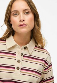 Beige gestreept polo-shirt met paarse, roze en bruine lijnen. Heeft een klassieke kraag en vier donkere knopen bij de sluiting. Zachte textuur.