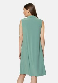 Ein ärmelloses, pastellgrünes Kleid mit klassischem Kragen, lockerem Schnitt und glattem Stoff, mit knielangem Saum und ohne sichtbare Verschlüsse.