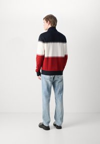 Giacca con zip a blocchi di colore che presenta sezioni blu scuro, bianco e rosso; tessuto morbido; colletto alto; polsini a costine; indossata con jeans azzurri chiari.