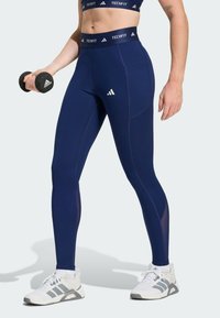 Leggings de sport bleu marine avec une taille haute, présentant une texture lisse, un tissu extensible et des coutures contrastantes. Logo à l'avant.