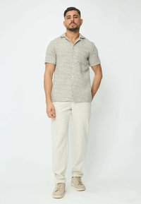 Chemise à manches courtes en tissu léger à motif, devant boutonné et col doux, associée à un pantalon crème et à des baskets beiges.