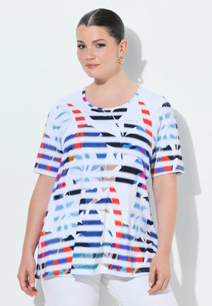 Kobieta o ciemnych włosach związanych w kok, nosząca złote kolczyki-koła oraz biały top z krótkim rękawem ozdobiony kolorowymi abstrakcyjnymi paskami i kształtami.