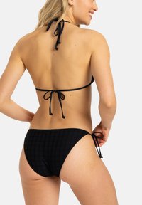 Svart bikini med en texturerad rutmönster, justerbara snören vid nacken och höfterna, med en stilren, minimalistisk design.