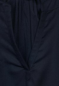 Merinovärinen kangas, jossa on V-neulemuotoilu. Sisältää kerrottu yksityiskohta kauluksessa ja erottuvan ompeleet reunoilla. Sileä rakenne.