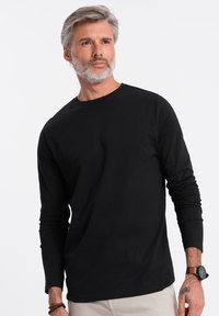 Schwarzes Langarm-T-Shirt aus weicher Baumwolle. Verfügt über einen runden Halsausschnitt und eng anliegende Ärmel. Einfaches, einfarbiges Design ohne Muster.