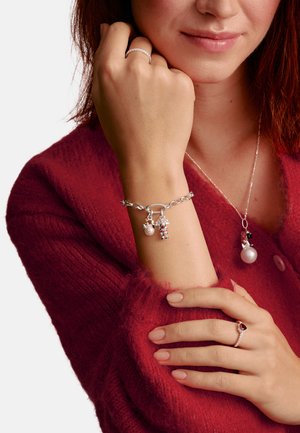 Silberarmband mit Perle und dekorativen Charms, getragen am Handgelenk, neben einer silbernen Halskette und einem Ring mit rotem Edelstein.