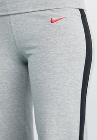 Harmaat collegehousut, jotka on valmistettu pehmeästä kankaasta, sisältävät punaisen Nike-logon ja mustan sivuvyöhykkeen korostuksena. Muotoiltu malli, jossa on joustava vyötärö.
