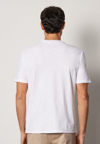 Vit t-shirt med kort ärm och rundad halsringning, tillverkad av lättviktigt tyg, med en slät yta och minimalistisk design.
