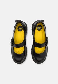 Black leather shoes with a round toe, adjustable strap, and yellow perforated insole. Textured rubber sole for grip.
