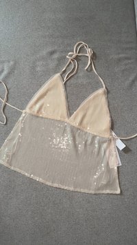 Beige driehoekige bikini-top met dunne bandjes; doorzichtige overlay met pailletten en een textuurpatroon; heeft een striksluiting en bijbehorende labels.