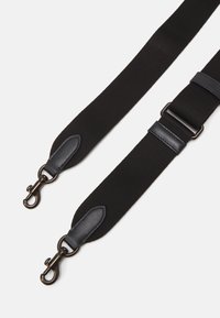 Correa ajustable negra hecha de nailon con acentos de cuero. Presenta clips de metal y una textura suave. Dos puntos de sujeción para versatilidad.