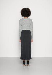 Un haut à manches longues gris côtelé associé à une jupe maxi noire, avec une texture lisse et des talons à bride de cheville en noir.