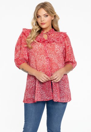 Rode blouse met patroon, een ruches-kraag en een sleutelgatdetail. Doorzichtig materiaal, ballonmouwen en een losse pasvorm. Gepaarde met blauwe jeans.
