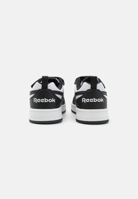 Baskets noir et blanc avec une tige en cuir lisse, un col rembourré et une semelle en caoutchouc texturé, présentant le logo "Reebok" sur le talon.