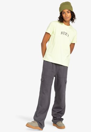 Light yellow Roxy t-shirt with a printed logo, paired with dark gray cargo pants featuring multiple pockets, and a green beanie.