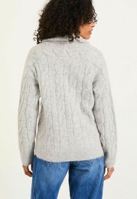 Kabelstrickpullover in Hellgrau mit hohem Kragen und strukturiertem Stoff. Der Rücken präsentiert einen gerippten Saum und eine lockere Passform.