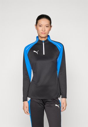 Black athletic half-zip top with blue side panels, long sleeves, and white logo on chest. Paired with matching black pants featuring blue accents.
