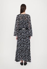Abito maxi floreale nero con maniche lunghe, caratterizzato da un orlo arricciato e una cintura nera. Il tessuto è trasparente con motivi di fiori blu e bianchi.