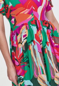 Kolorowa sukienka z kwiatowym wzorem w odcieniach zieleni, różu, czerwieni i niebieskiego. Wykonana z lekkiego materiału, z rozkloszowanym, plisowanym krojem spódnicy.