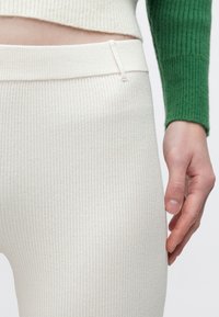 Ribbede cremefarvede leggings med høj talje. Blød tekstur, der er tydelig, kombineret med en grøn ribbet sweater, der ses delvist øverst.