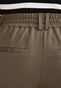 Pantalon vert olive avec une taille élastique, présentant une texture lisse et de petites poches arrière, conçu pour le confort et la facilité de port.