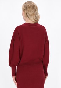 Bordeaux gestrickter Pullover mit Ballonärmeln, gerippten Bündchen und Saum. Weicher Stoff, entspannter Schnitt und Rundhalsausschnitt. Schlichtes, einfarbiges Design.