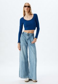 Pitkähiha, pyöreäkauluksinen crop-top kirkkaan sinisestä ribbineuloksesta, yhdistettynä leveälahkeisiin vaaleansinihin farkkuihin. Tosanat täydentävät asua.