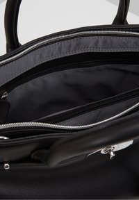 Sac à main en cuir noir ouvert pour montrer l'intérieur spacieux avec deux compartiments zippés et des poignées rembourrées.