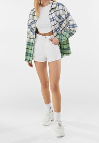 Grön och vit rutiga flanellskjorta, vit kortärmad topp, vita denimshorts, vita sneakers och vita ankelsockor. Avslappnad outfit med lager.