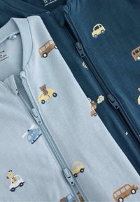 Δύο φερμουάρ ολόσωμες φόρμες: ανοιχτό μπλε με εκτυπωμένα οχήματα και ζώα, σκούρο μπλε με σχέδια οχημάτων. Και οι δύο κατασκευασμένες από μαλακό ύφασμα.