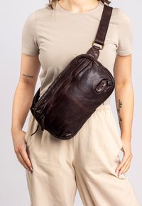 Brown leather crossbody bag with zip closure, rectangular shape, and adjustable strap, featuring a subtle embossed logo detail on the side.