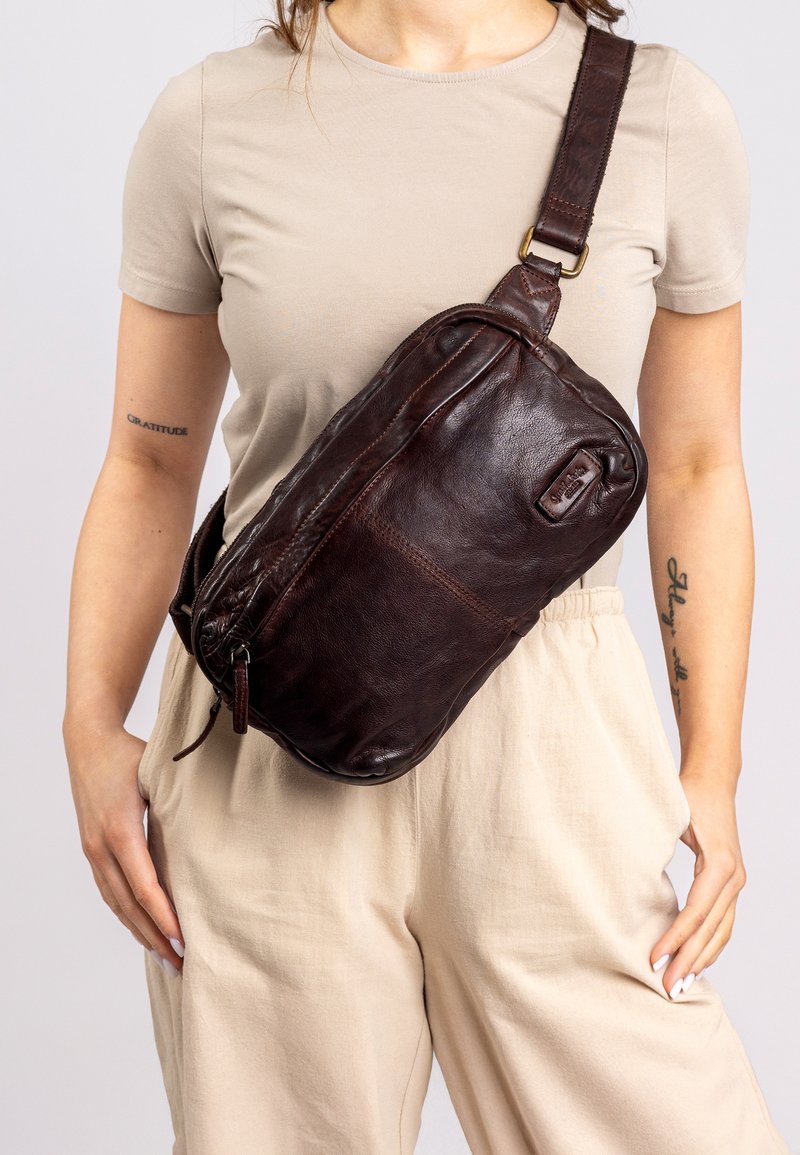 Brown leather crossbody bag with zip closure, rectangular shape, and adjustable strap, featuring a subtle embossed logo detail on the side.