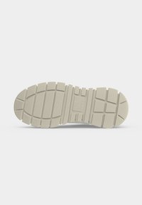 Semelle d’une botte beige clair avec des motifs de bande de roulement profonds rectangulaires et carrés pour l’adhérence et la stabilité sur une surface plane.