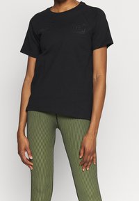 Camiseta de algodón negra con textura acanalada, con escote redondeado y mangas cortas. Acompañada de leggings a rayas verdes.
