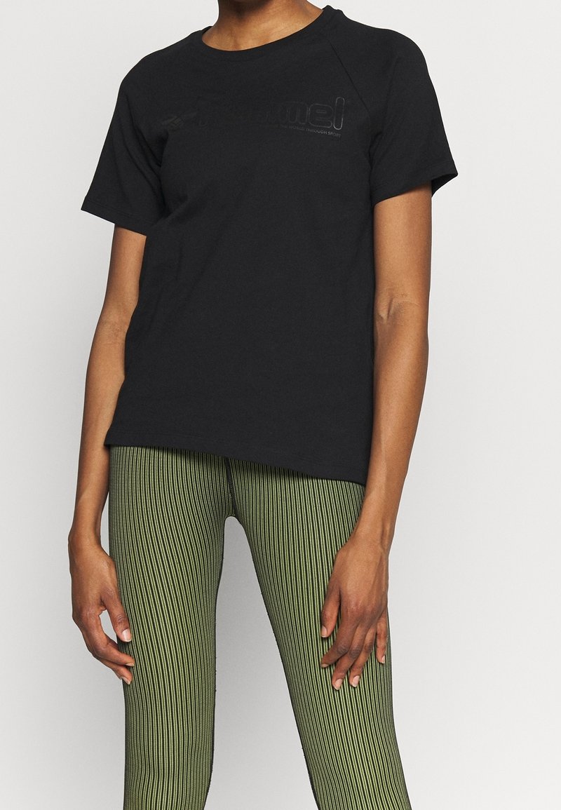 Camiseta de algodón negra con textura acanalada, con escote redondeado y mangas cortas. Acompañada de leggings a rayas verdes.