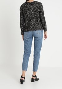 Czarny i biały sweter o fakturze z długimi rękawami, w połączeniu z jasnoniebieskimi dżinsami i czarnymi sandałami na wysokim obcasie.