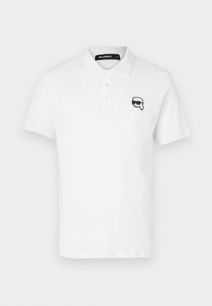 Polo shirt bianca con maniche corte, colletto con tre bottoni e un logo cartoon ricamato nero sul lato sinistro del petto.