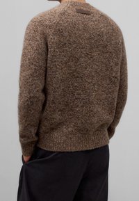 Brązowy sweter z teksturowanym splotem, z okrągłym dekoltem, prążkowanym dołem oraz małą skórzaną metką na karku. Luźny fason z długimi rękawami.