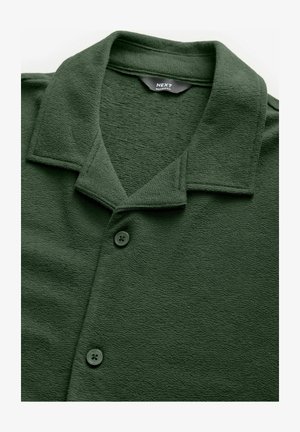 Ciemnozielona koszula o strukturalnym materiale, z kołnierzykiem, trzema guzikami i luźnym fasonem. Metka informuje "NEXT Relaxed Fit."