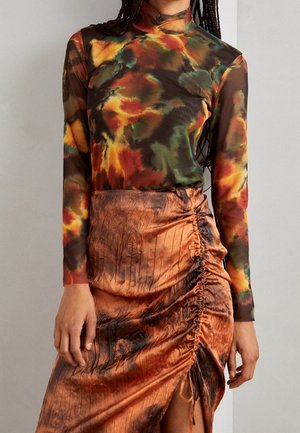 Top z długim rękawem w stylu tie-dye w jesiennych kolorach, zestawiony z marszczoną, spaloną pomarańczową satynową spódnicą z rozcięciem z przodu.