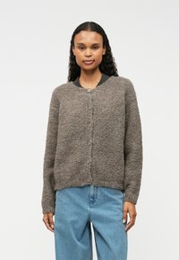 Cardigan gri, cu textură, cu guler rotund și închidere cu nasturi, purtat cu blugi de un albastru deschis. Material moale și croială lejeră.