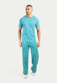 Turquoise kortärmad blouse en bijpassende losse broek van zachte stof. Heeft een minimalistisch ontwerp en een klein logo op het shirt.