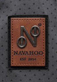 Brown leather patch with embossed logo "N" and "NAVAHOO EST 2014"; black stitching on a textured gray background with small pattern details.