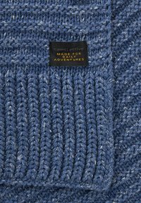 Gebreide blauwe trui met een gestructureerd oppervlak, voorzien van een zwart label met de tekst "camelactive MADE FOR DAILY ADVENTURES" in oranje letters.