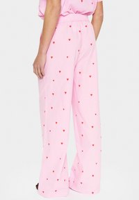 Roze wijde broek gemaakt van lichtgewicht stof, met een patroon van kleine rode harten die over het oppervlak zijn verspreid. Elastische tailleband zichtbaar.