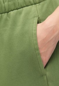 Green cotton shorts with a textured fabric. Features an elastic waistband and side pockets for functionality.