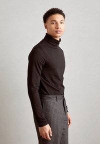 Svart høyhalset genser sammen med grå stripete bukser. Stoffet ser glatt ut, med en tettsittende design og middels tykkelse.