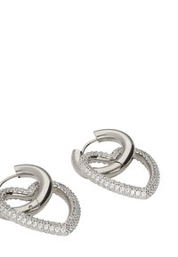 Metaliczne kolczyki w kształcie skręconego serca, ozdobione przezroczystymi kryształkami. Posiadają błyszczące srebrne wykończenie i mechanizm zapięcia na klips.